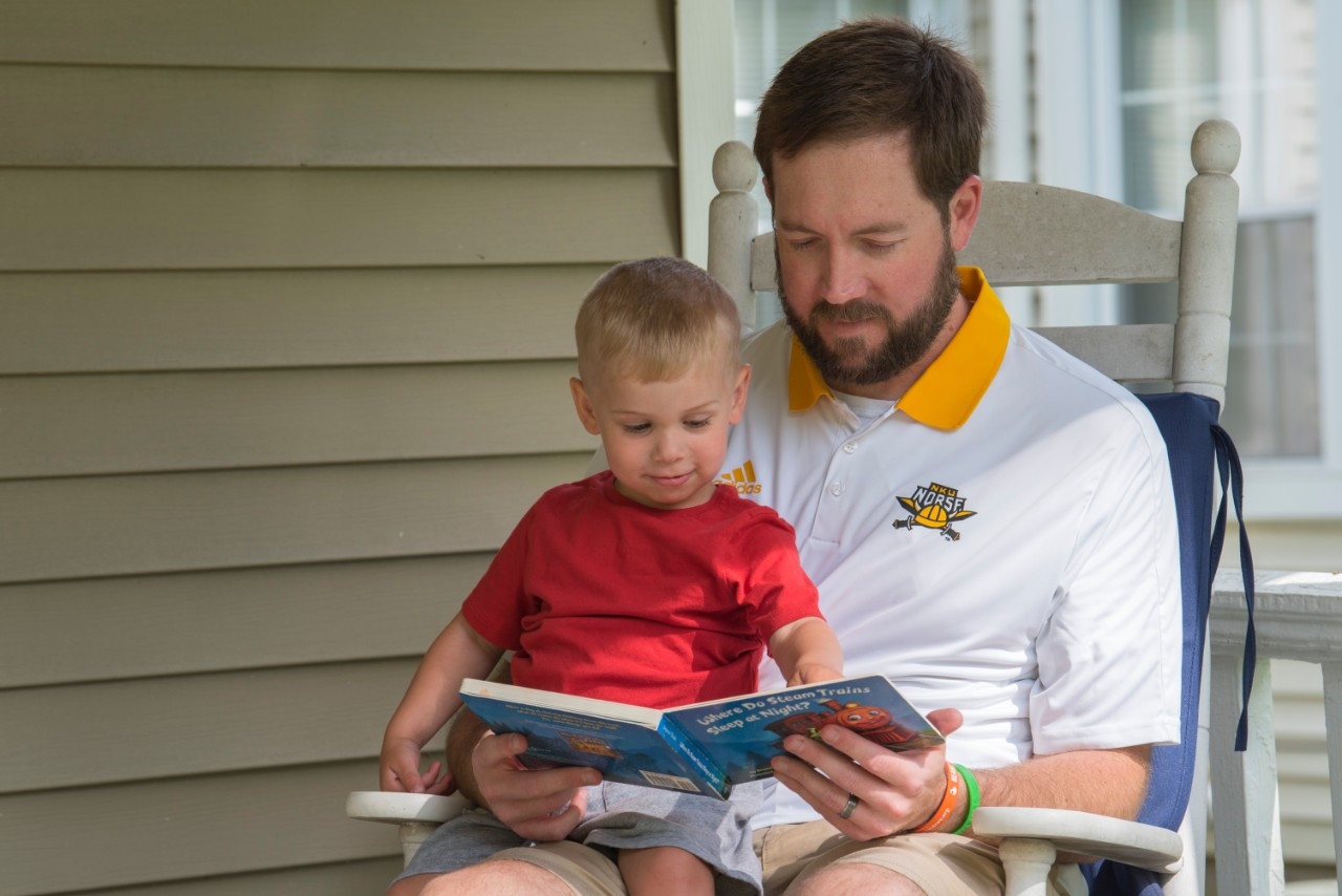 Person wearing NKU polo, reading book to small child.