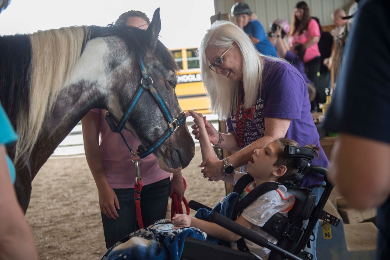 Person assisting child in a wheelchair pet a horse.