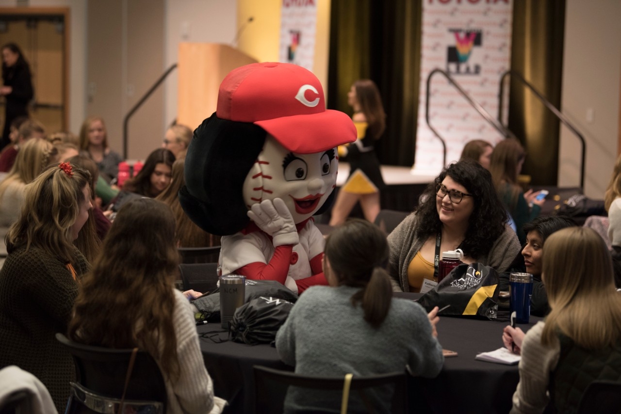 Students sitting at a table with the Rosie Red mascot.