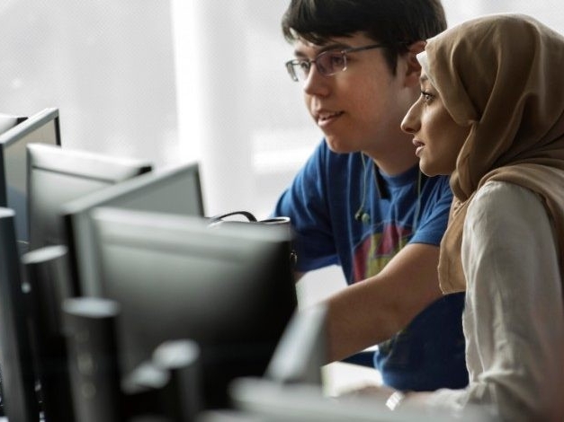 Two students looking at computer screen together in a computer lab.