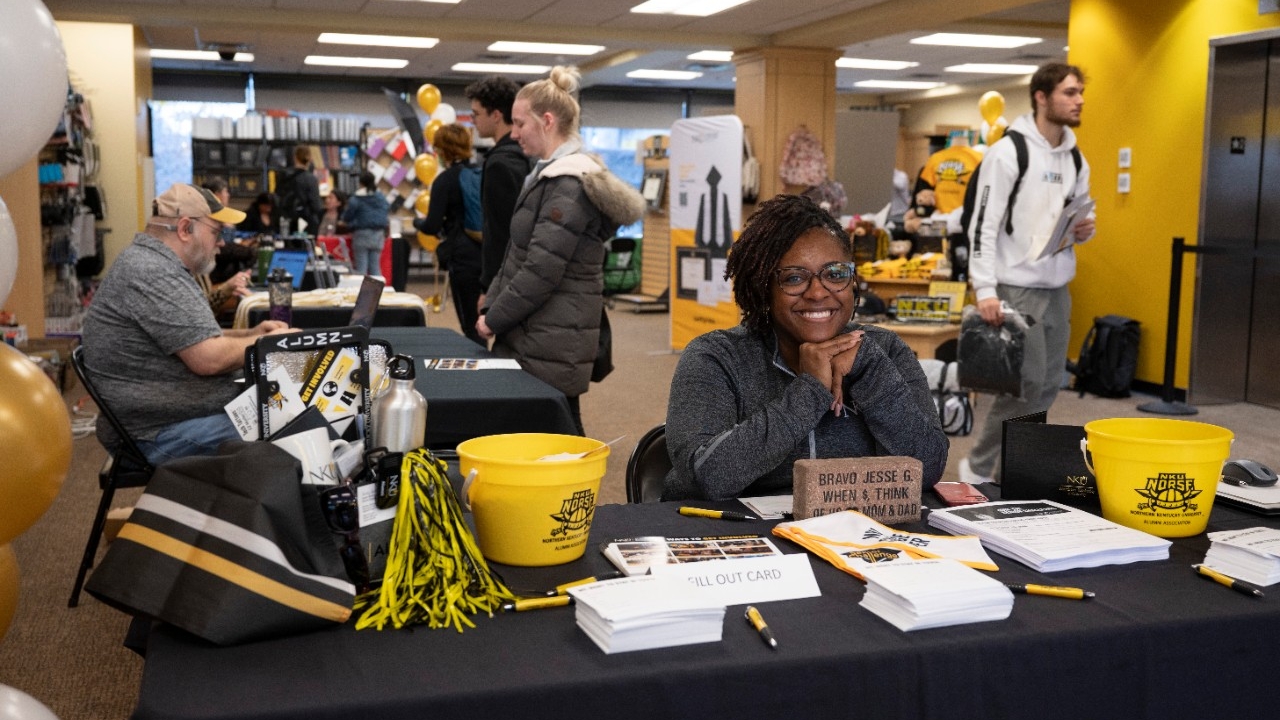 NKU Bookstore staff member smiling at the welcome table for the Graduation Fair.