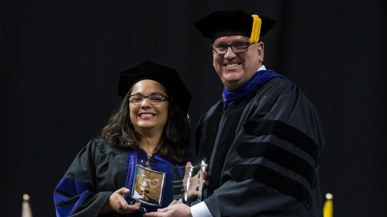 Faculty member posing with a student on the graduation stage.