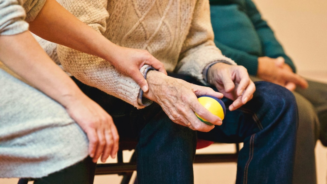Woman helping a senior man as he squeezes a stress ball.