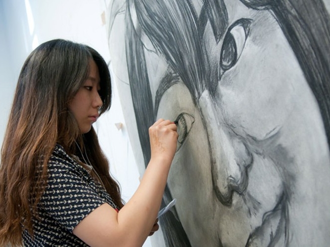 Student working on a large portrait of a face.