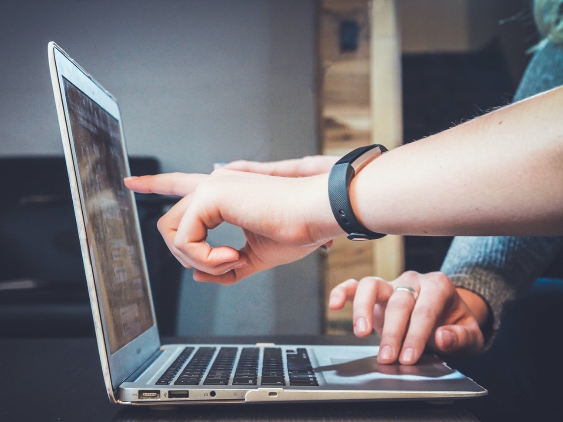 Hand pointing to a laptop screen.