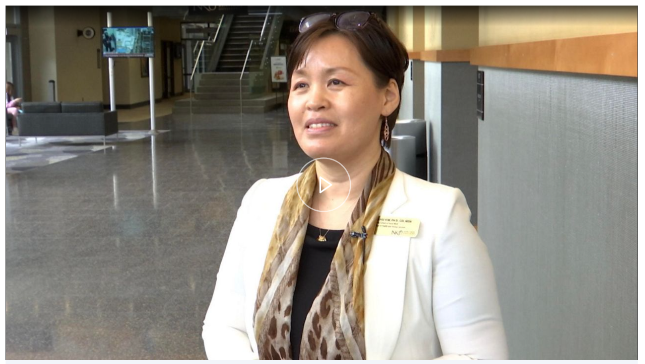 Dr. Suk-hee Kim standing in wide hallway talking to a news reporter off-screen.