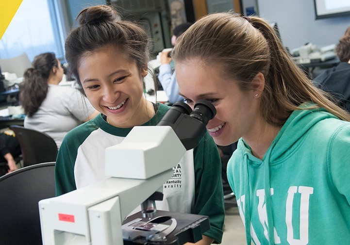 Two NKU students looking through a microscope.