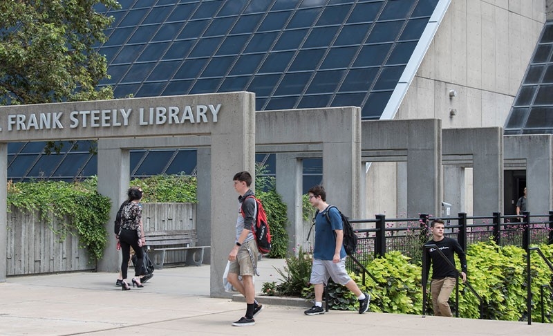 Exterior of Steely Library building with people walking on sidewalks.