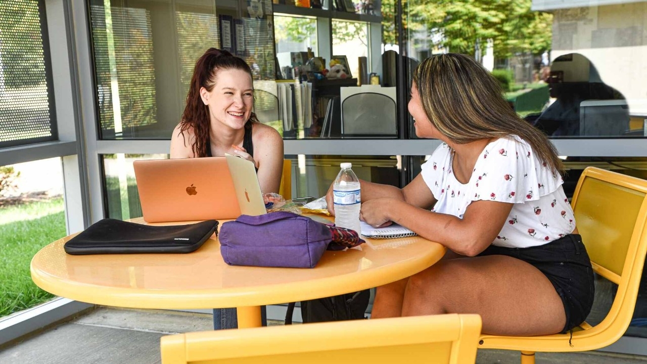 Students smiling while sitting down around a laptop