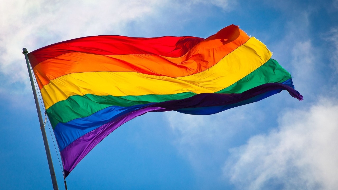Pride flag and bright blue skies with some wispy clouds in the background