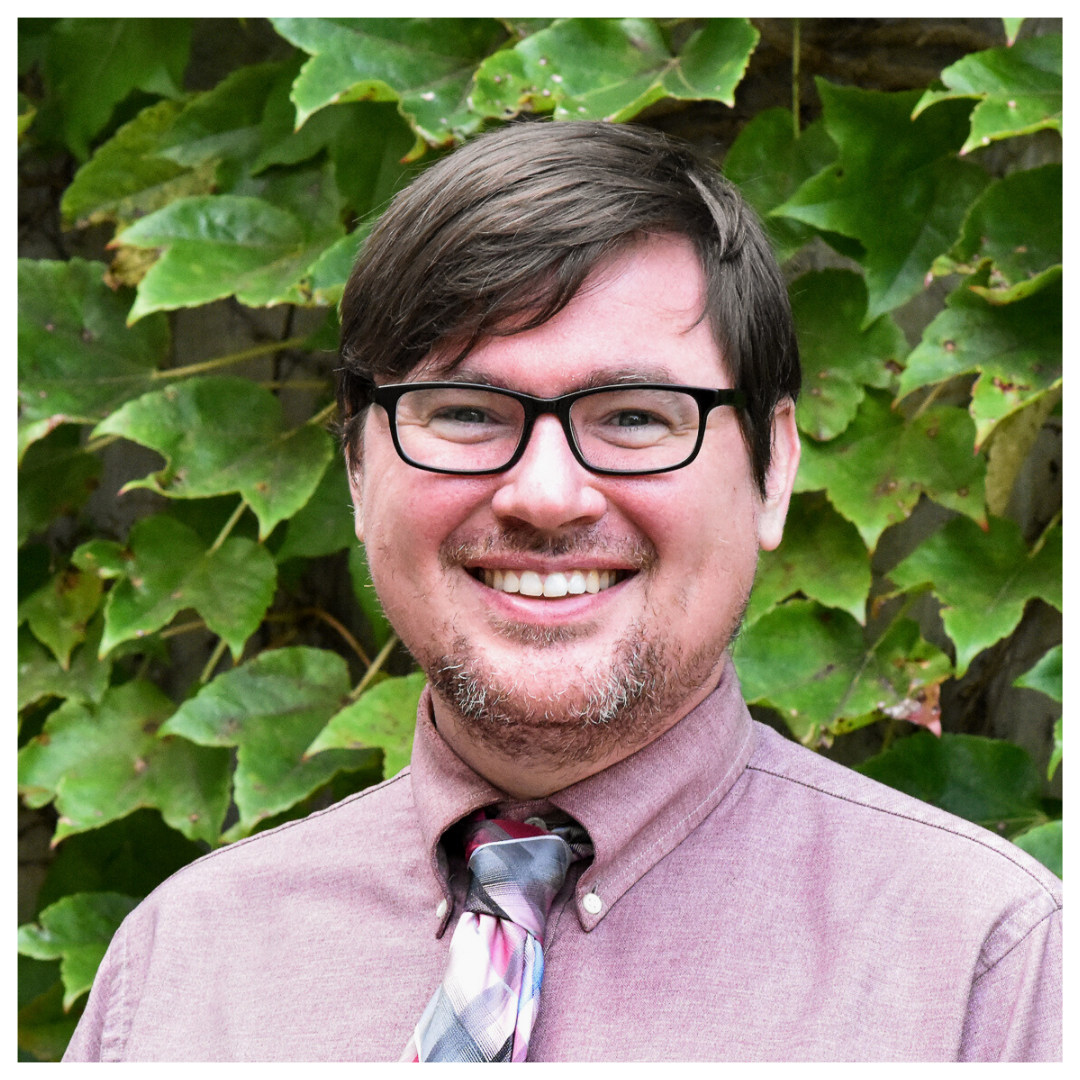 Headshot of Christian Sheehy in front of green vines