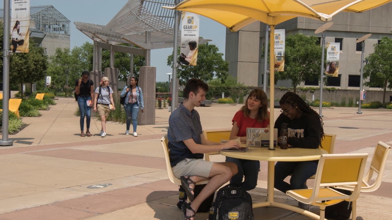 Students sitting outside of Steely Library at a yellow table with "GEAR UP" banners in the background.