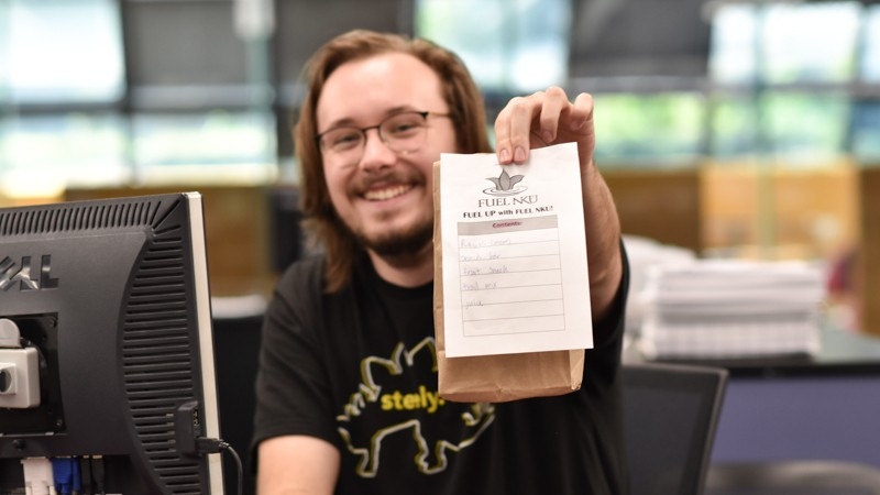 Steely student employee displaying a FUEL UP bag at the 3rd floor public services desk. 