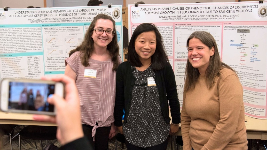 Students smiling in front of a research poster. 