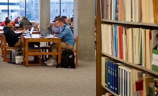 Periodicals on shelves and students sitting at tables in the background
