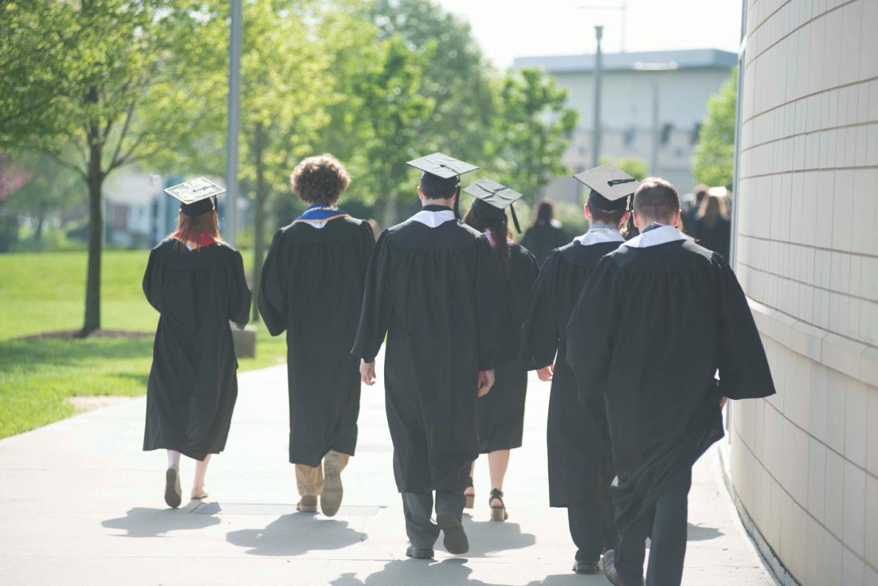 Graduates walking on campus dressed in regalia