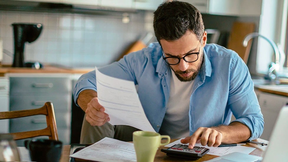 Man working on laptop and looking at paper bills