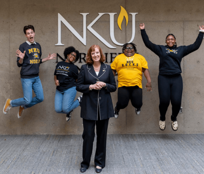 4 students jumping in air behind NKU President Cady Short-Thompson