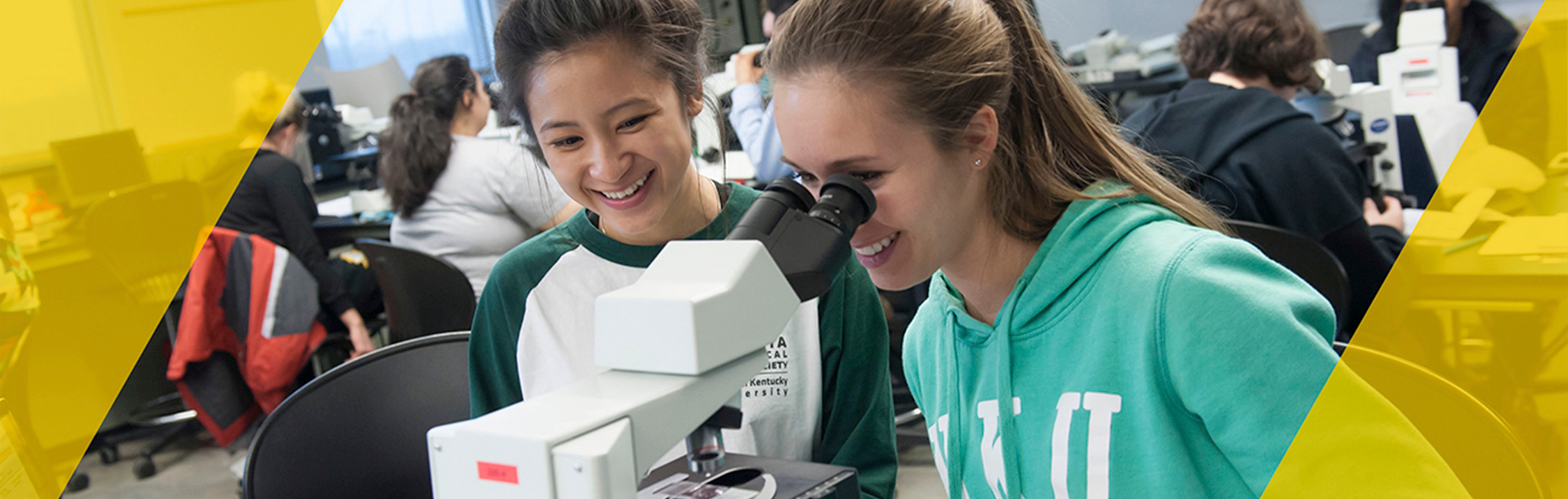 Two students look through microscope
