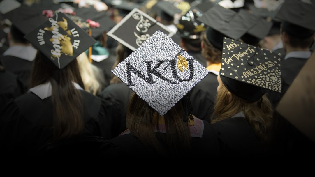 Graduating students gathered together in a group. One student's graduation cap has the NKU logo displayed. 
