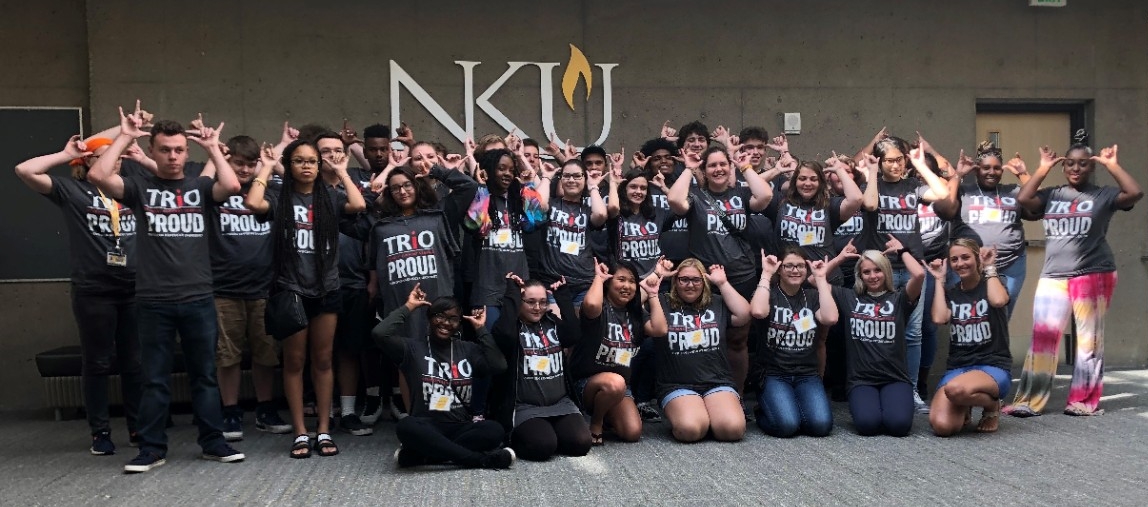 Group of students in front of an NKU sign giving the Norse Up hand signal
