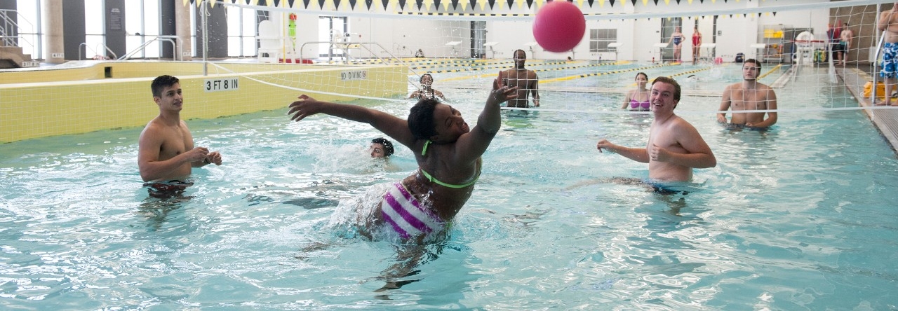A variety of students in the pool playing water volleyball. 