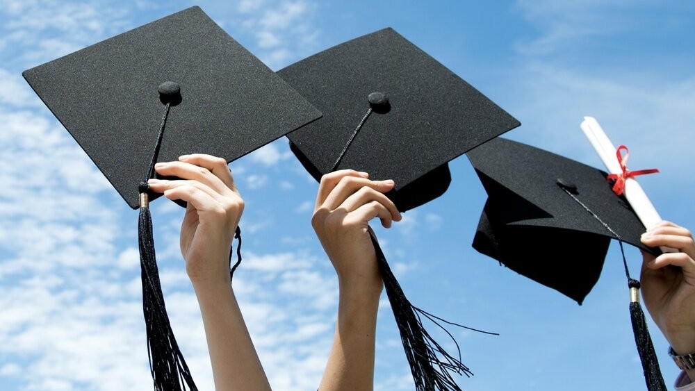 Hands tossing graduation caps and a rolled diploma into the air