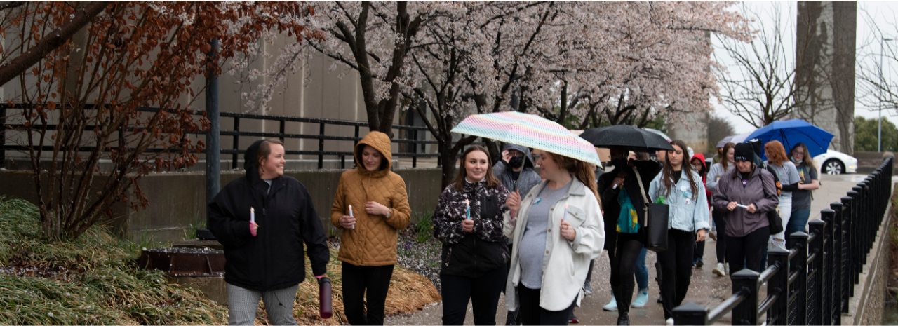 People walking on campus holding candles and umbrellas