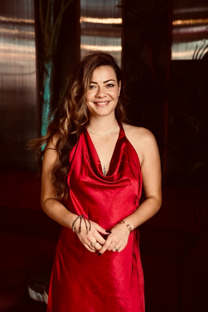 Woman in red dress standing in front of a dark background.