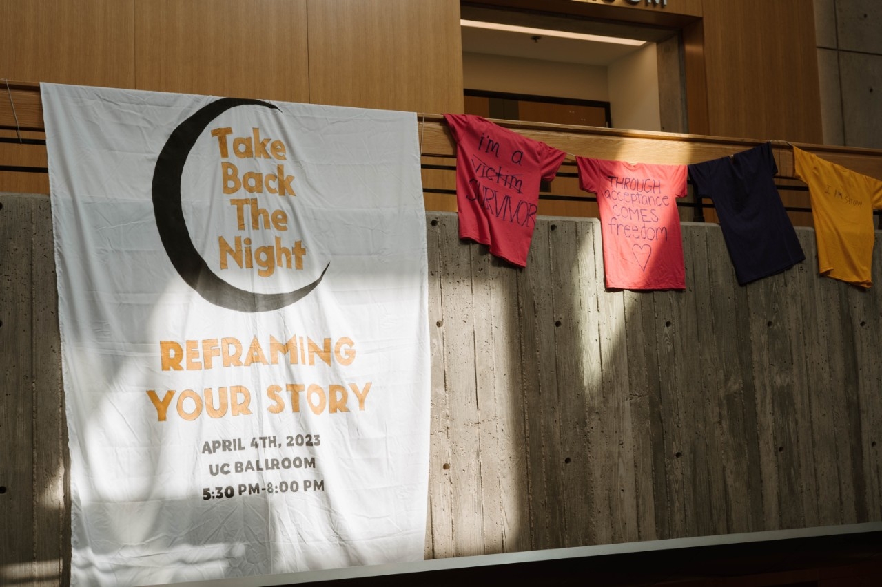 Take Back the Night banner hanging next to colorful t-shirts