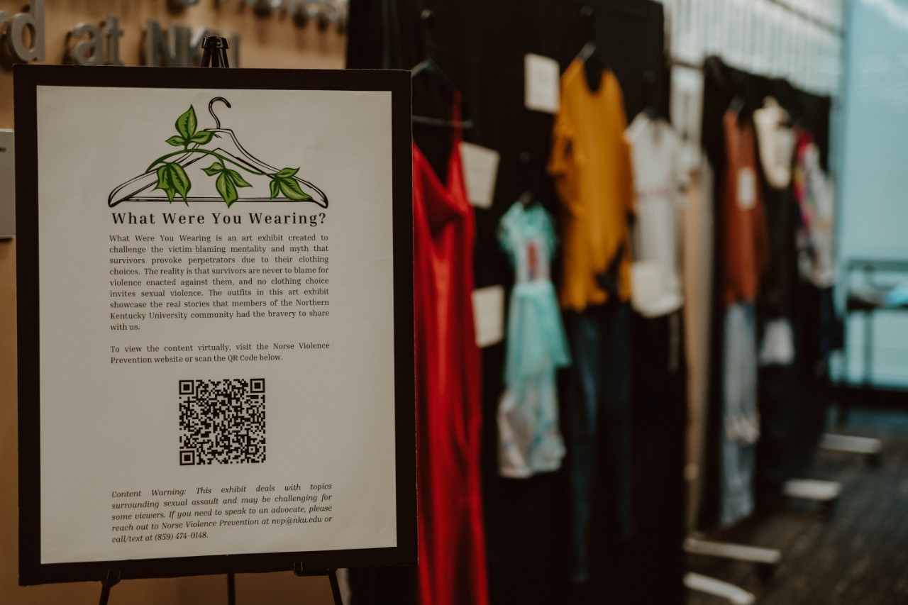 Event sign for What Were You Wearing exhibit with clothing display in background