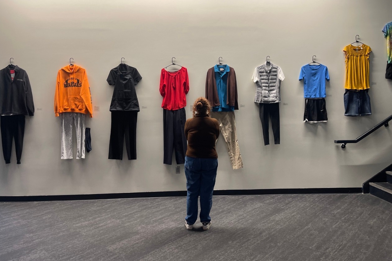Person standing in front of clothing displayed on white wall
