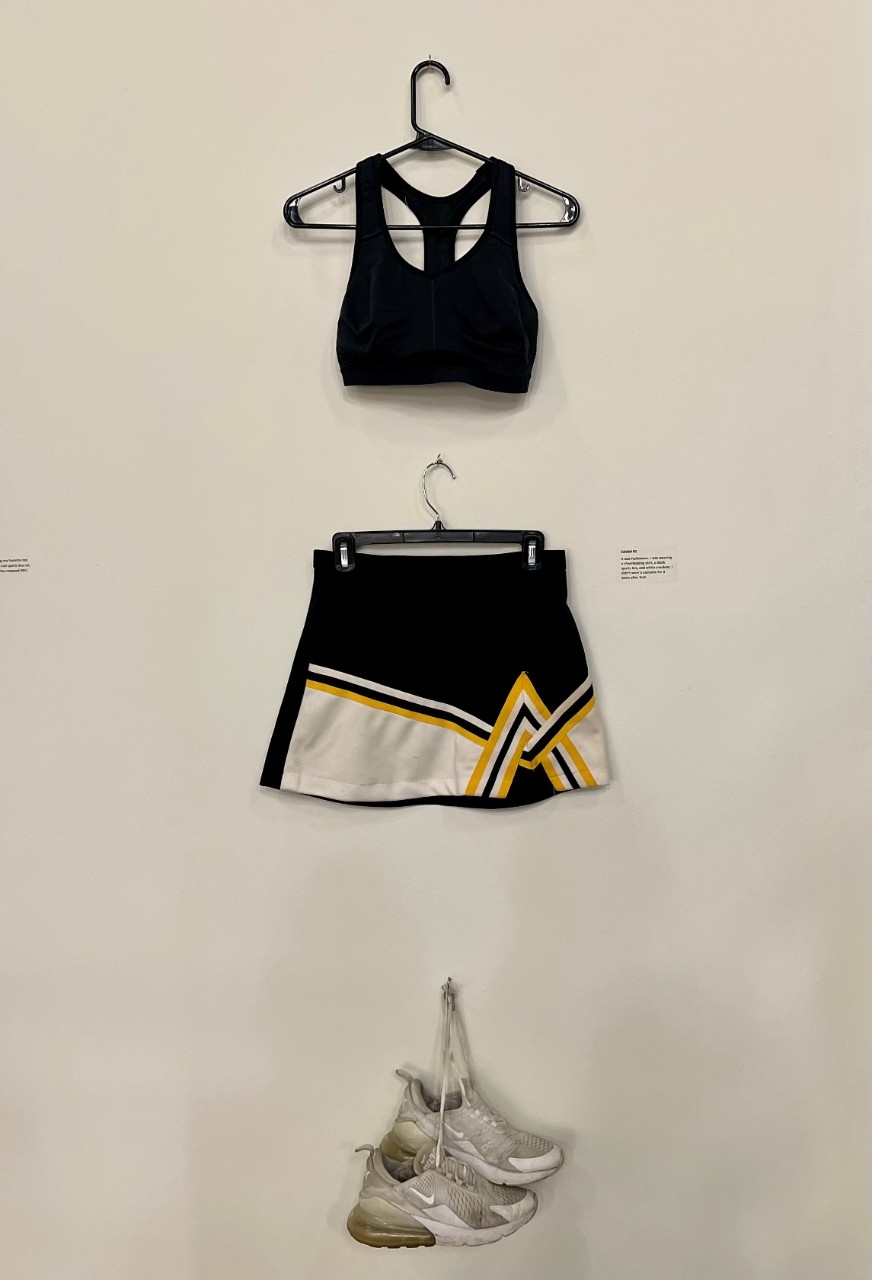 Black sports bra, Black Cheerleading Skirt with a white stripe and yellow stripes on the bottom. White Sneakers