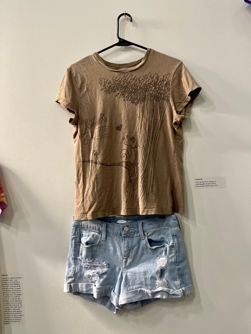 Small brown T-Shirt with an image of a squirrel in a tree, "Hug A Tree" Written on the shirt. Small jean shorts with small rips