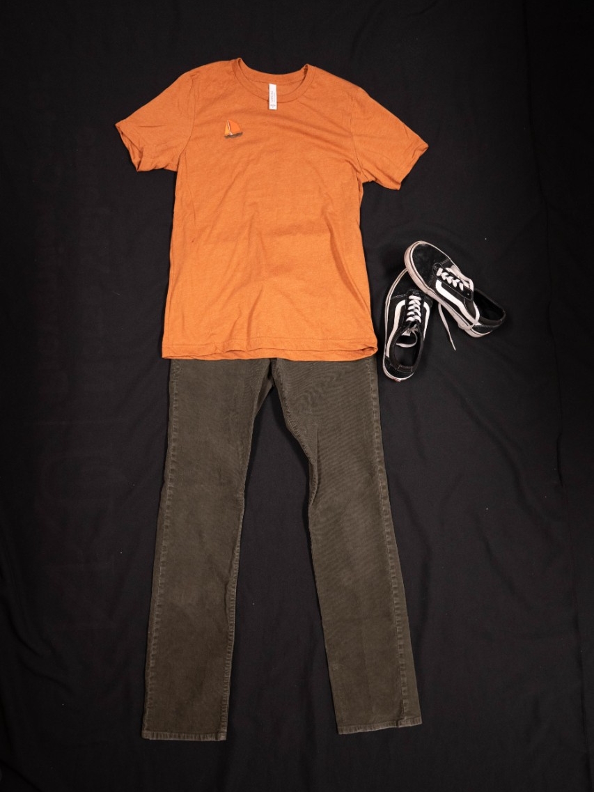 Exhibit displays a light brown shirt with an orange embroidered boat and green corduroy pants. 