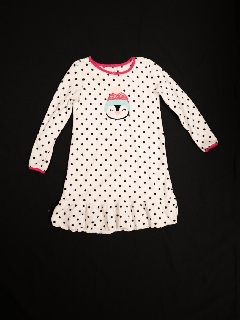 Exhibit displays a white fleece child’s nightgown with black polka dots and a penguin in the center. 