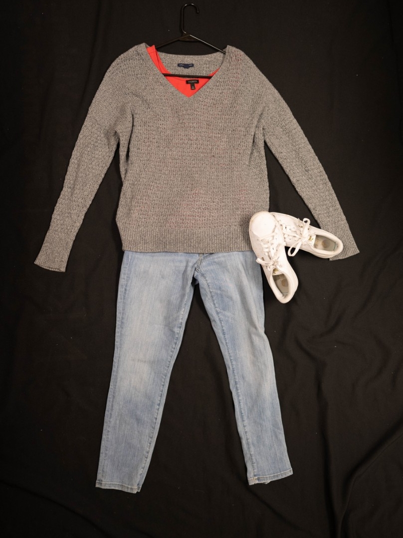 Exhibit displays a red tank top with an oversized gray sweater, a standard pair of jeans, and white sneakers. 
