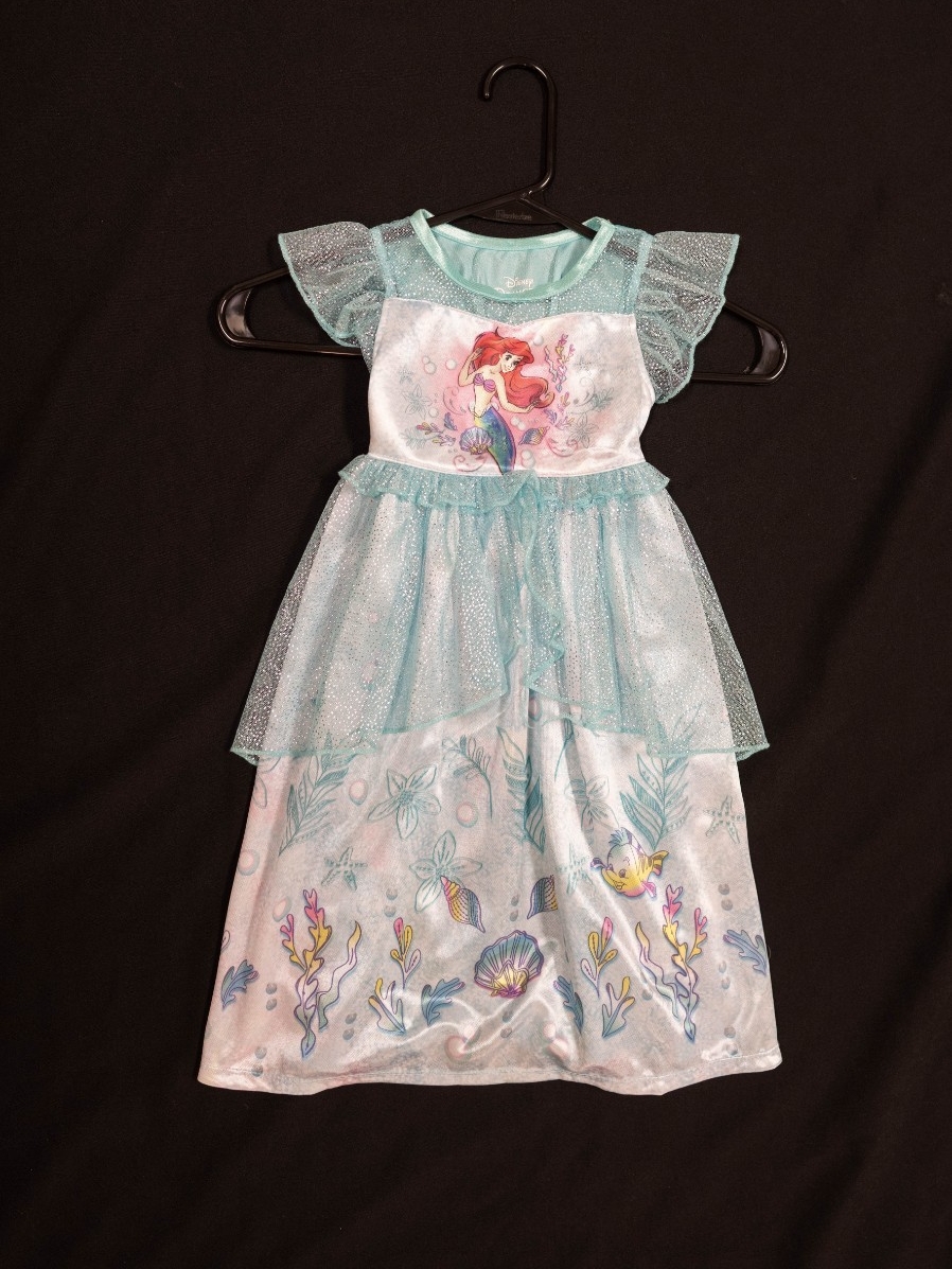 Exhibit displays a teal child’s nightgown with ruffles. The top of the nightgown displays the little mermaid and the bottom features an ocean scene.