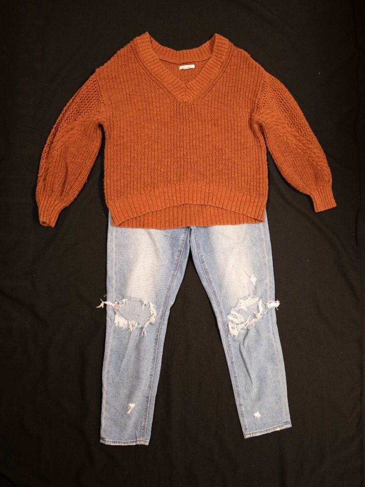 Exhibit displays a burnt orange sweater with ripped skinny jeans.