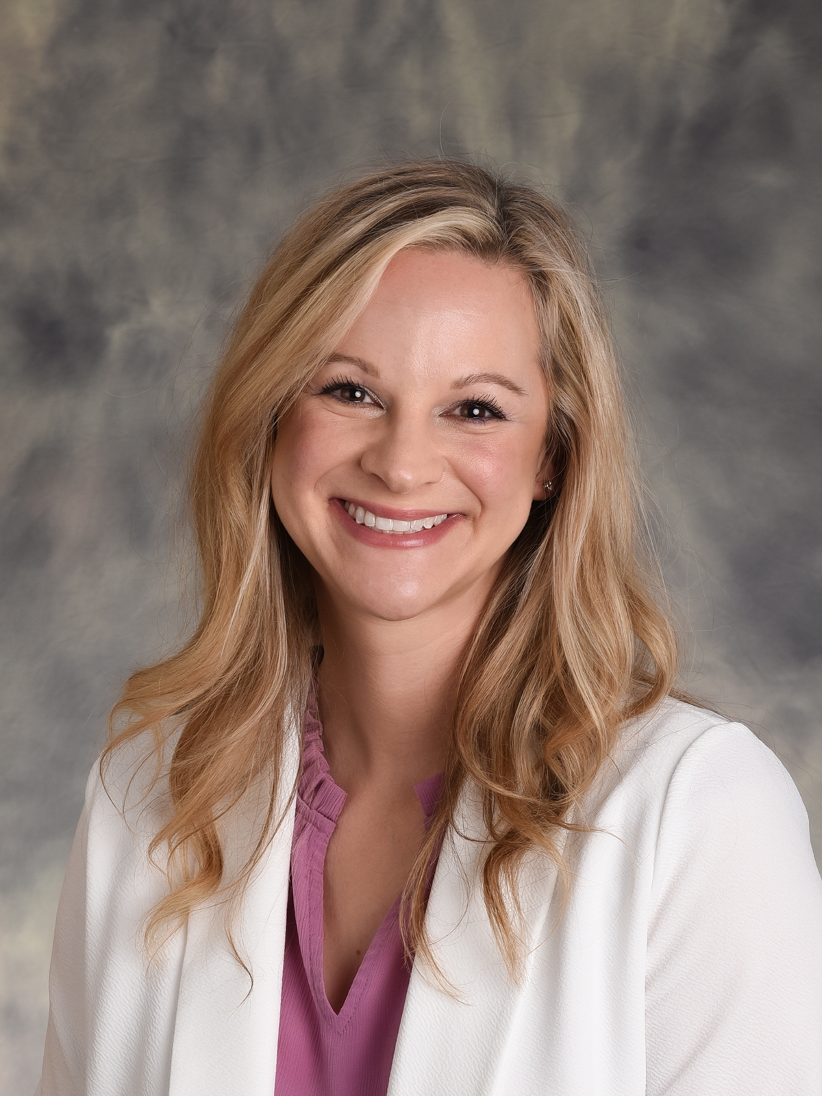 Photo of a brown haired, Caucasian, young professional woman, smiling, in professional attire.