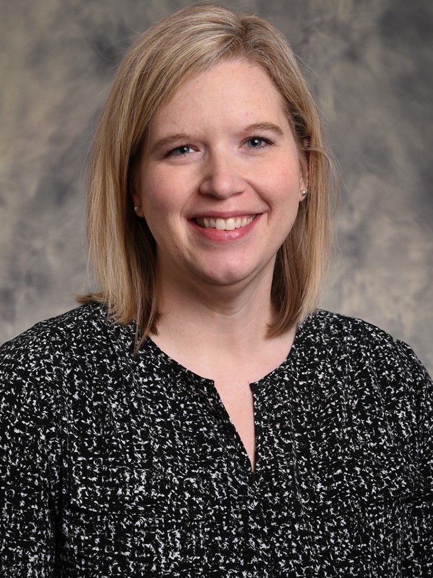 Photo of a blonde haired, Caucasian, young professional woman, smiling, in professional attire.