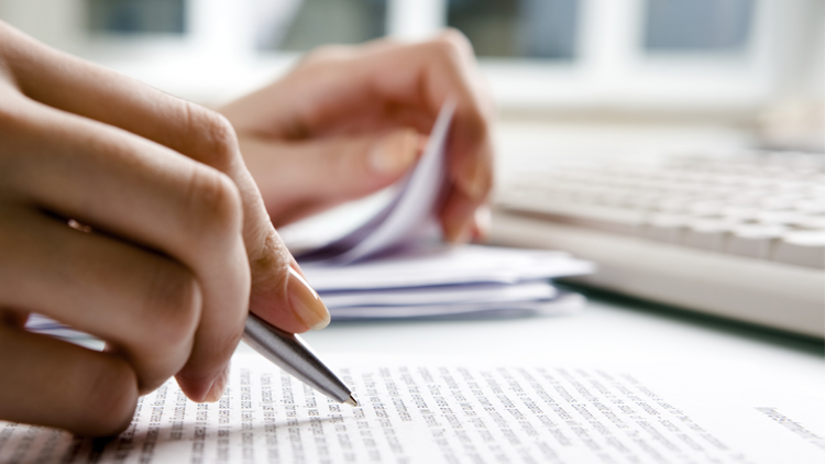 Person holding a pen and thumbing through papers.