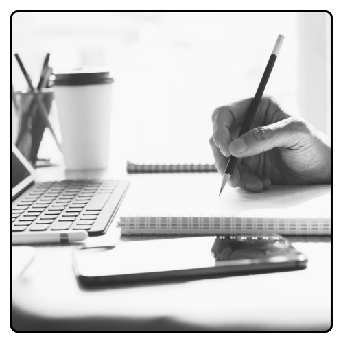 Person writing in a notebook and looking at a laptop