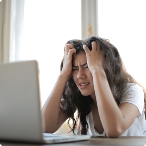 Female college student clutching her hair and looking stresshed at a laptop