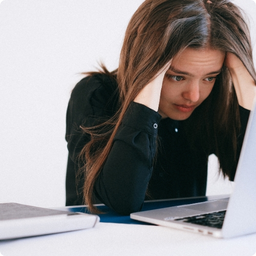 female student looking stressed and holding her head while staring at a laptop