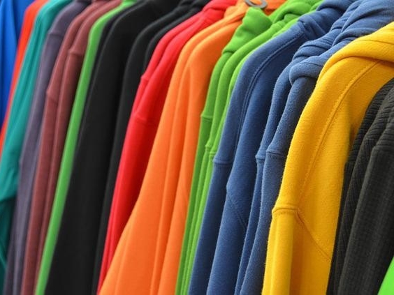 Row of colorful sweaters hang inside a closet.