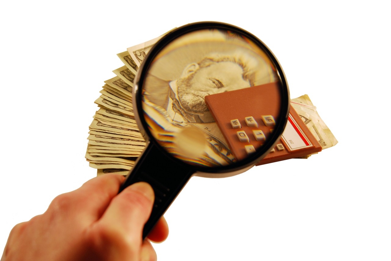 Person holding a magnifying glass to dollar bills