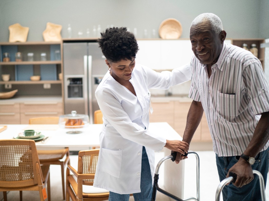 Nurse assisting an elderly man using a walker.