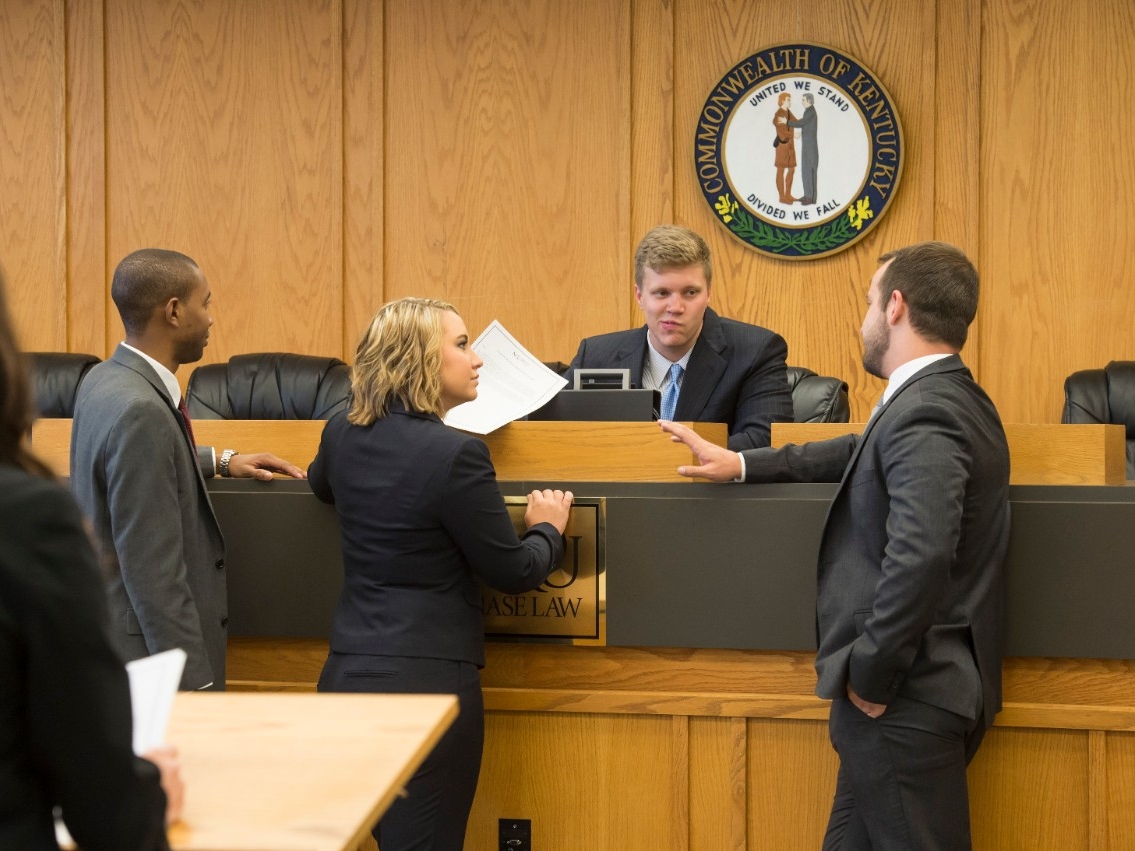 Three lawyers speaking with a judge inside a Kentucky courtroom.