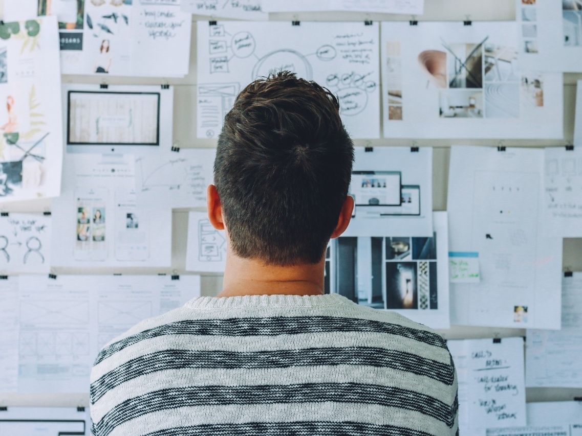 Man standing in front of a cork board reviewing pieces of paper to plan a concept